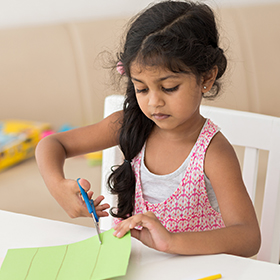 Little girl cutting paper with scissors
